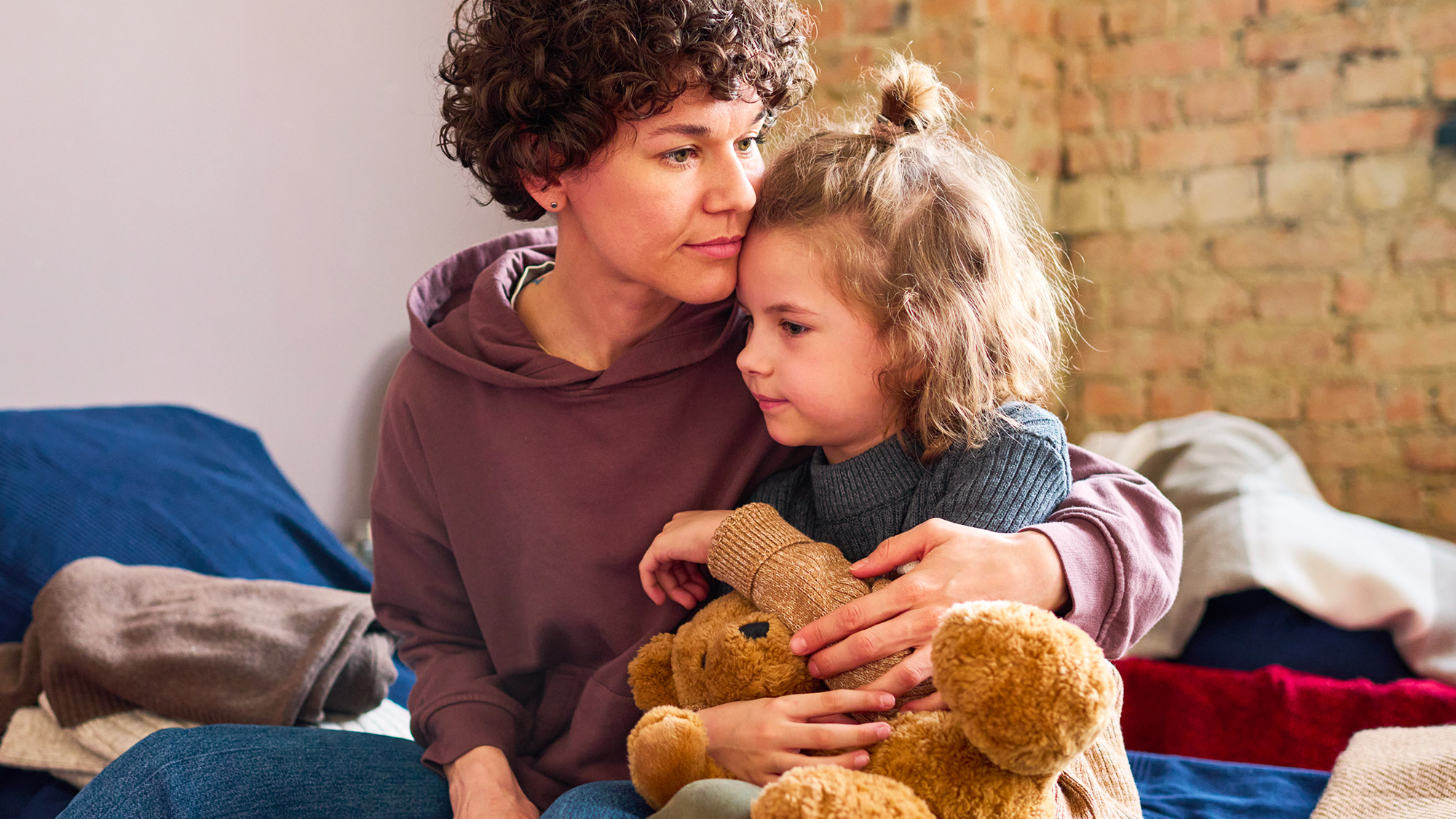 A mom hugging her daughter and her bear