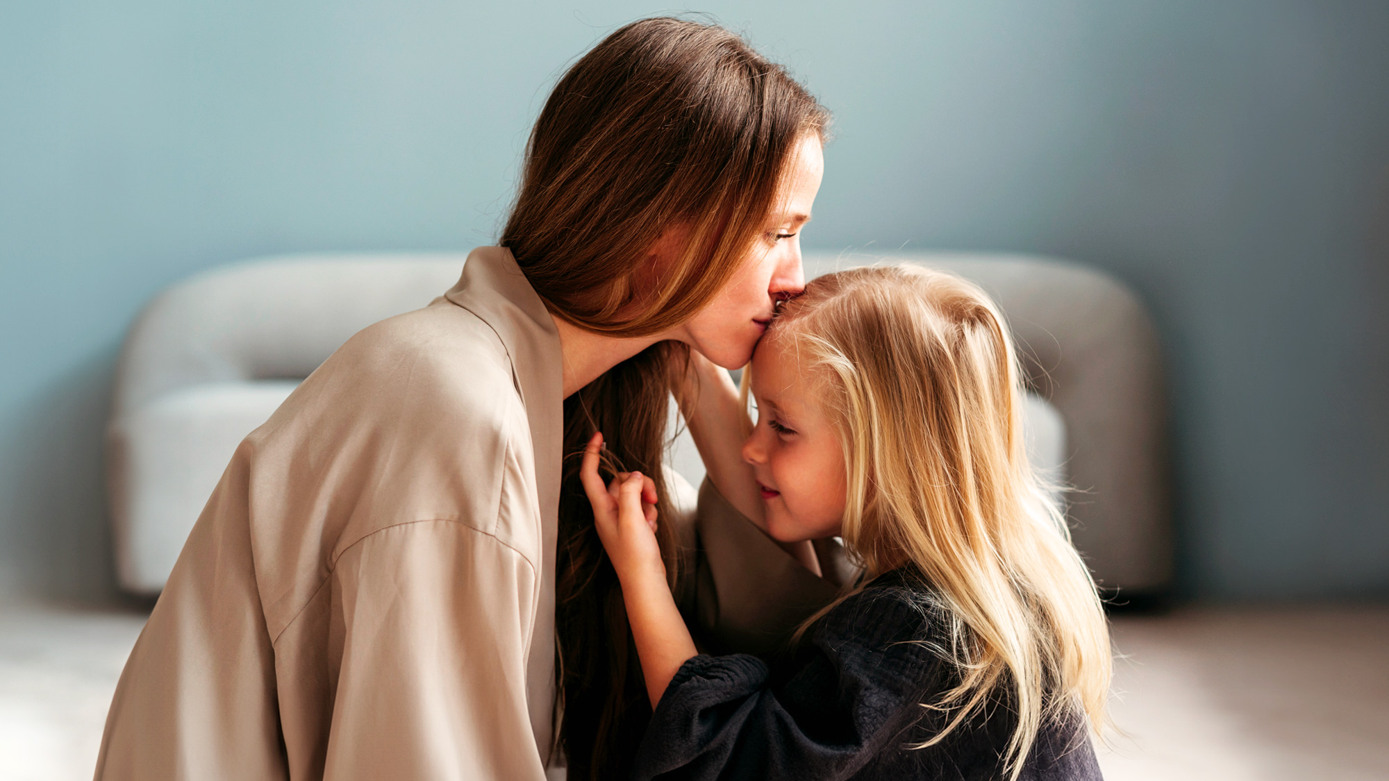 a mom kissing her daughter on her forehead